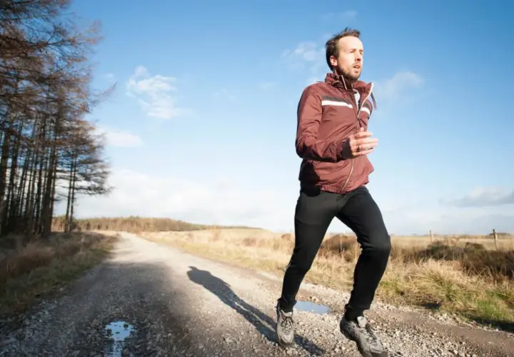 Mann joggt bei 10 Grad auf einem Feldweg. Er trägt eine leichte Jacke und lange Hose, ideal zum **was anziehen joggen 10 grad**.