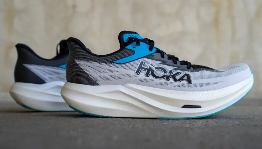 Zwei Hoka Rocket X3 Laufschuhe in Grau mit blauen Akzenten und weißer Sohle stehen nebeneinander.