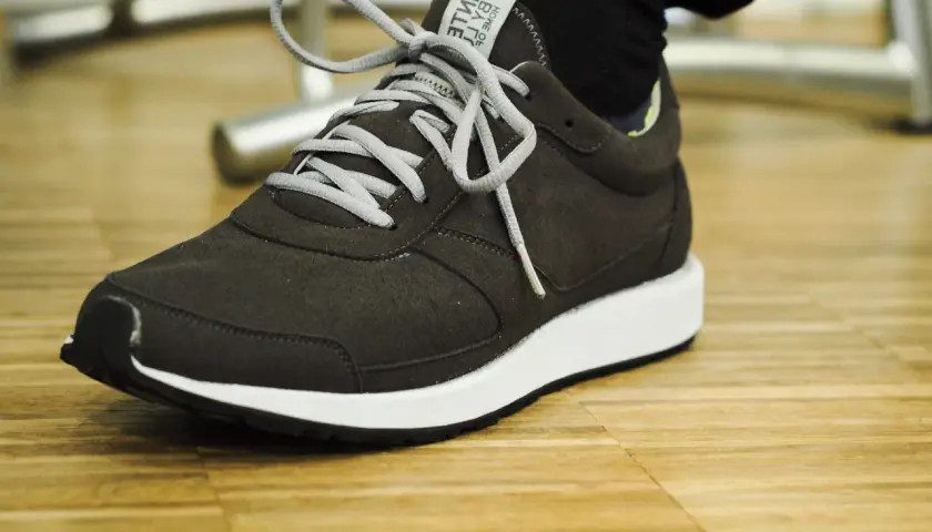 Dunkelgrauer Sneaker mit weißen Schnürsenkeln auf Holzfußboden. Gute Lunge Schuhe Erfahrungen für den Alltag.