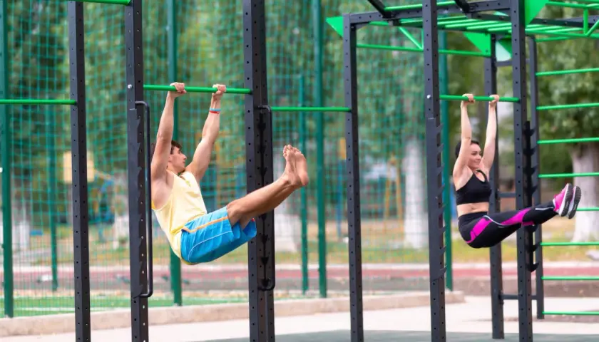 Mann und Frau trainieren Beinheben an einer Calisthenics-Anlage. Ein effektiver Teil ihres Trainingsplans.