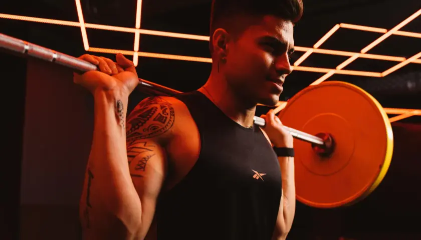 Ein Mann mit Tattoos und einem schwarzen Tanktop hebt eine Hantel. Er schwitzt und konzentriert sich auf sein Dropsatz Training.