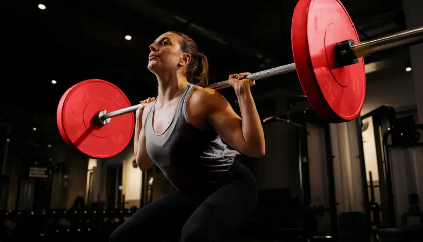 Frau mit Langhantel im Fitnessstudio, konzentriert auf Kniebeugen für Muskelaufbau.