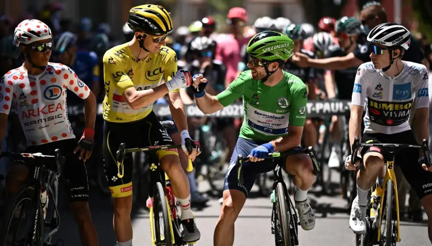 Radfahrer mit gelbem Trikot und grünen Trikot stoßen Fäuste. Ein Radfahrer im gepunkteten Trikot und einer im weißen Trikot stehen daneben. Ein Moment der Anerkennung beim Tour de France Gesamt.