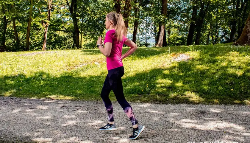 Frau läuft im Wald, um sich aufzulaufen. Sonnenschein und grüne Bäume schaffen eine idyllische Kulisse für ihr Training.