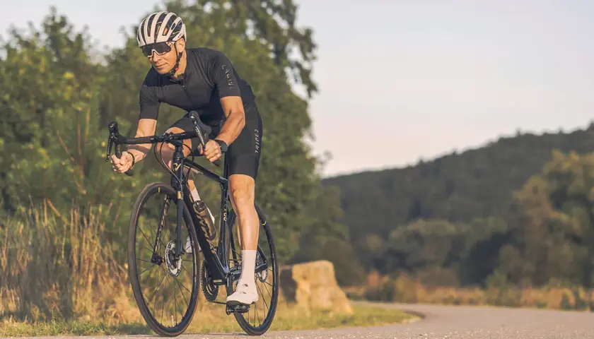 Mann auf Rennrad mit Helm und Brille fährt auf asphaltierter Straße durch hügelige Landschaft. Tolle Rennrad Tipps für deine nächste Tour!