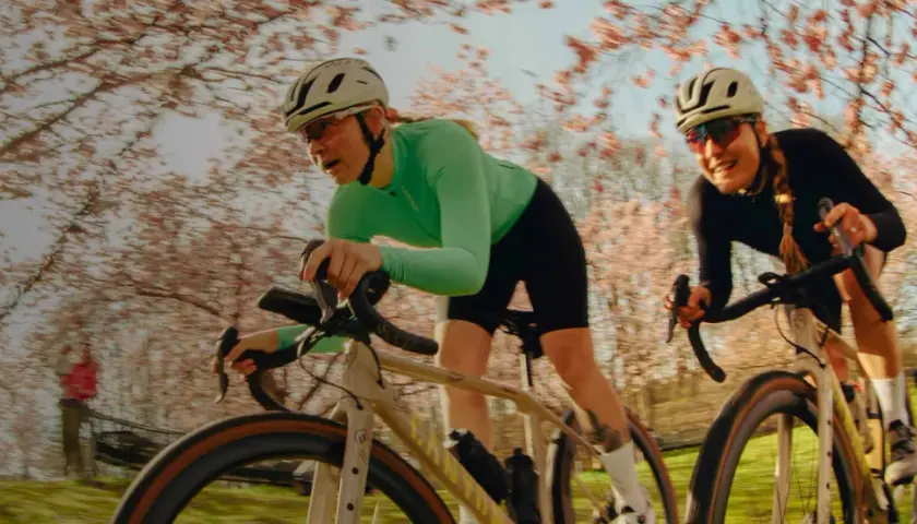 Zwei Frauen auf Rennrädern fahren durch eine blühende Kirschbaumallee. Sie sind Teil einer lebendigen Fahrrad-Community, die die Natur genießt.