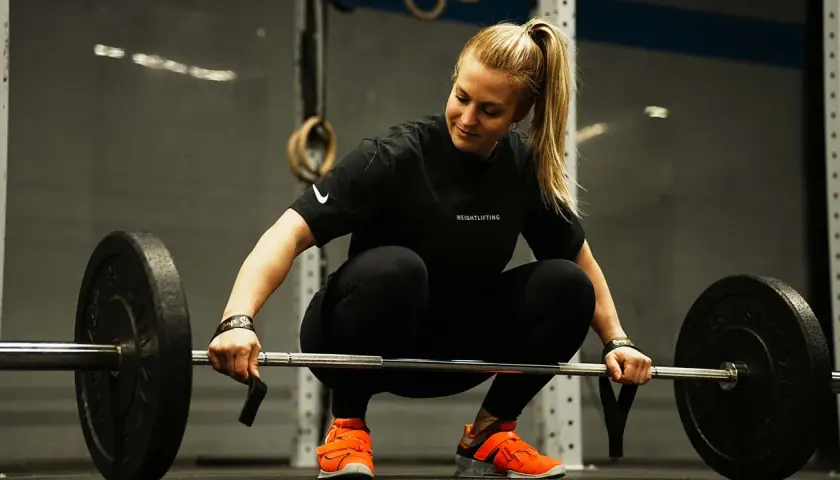 Eine Frau im Fitnessstudio bereitet sich auf das Gewichtheben vor. Eine Woche Trainingspause kann sinnvoll sein, um sich zu erholen.