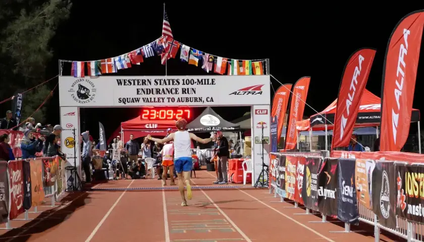 Läufer erreicht das Ziel beim Western States 100-Mile Endurance Run. Die Ziellinie ist mit Flaggen geschmückt, die an einen Ultramarathon in Deutschland erinnern.