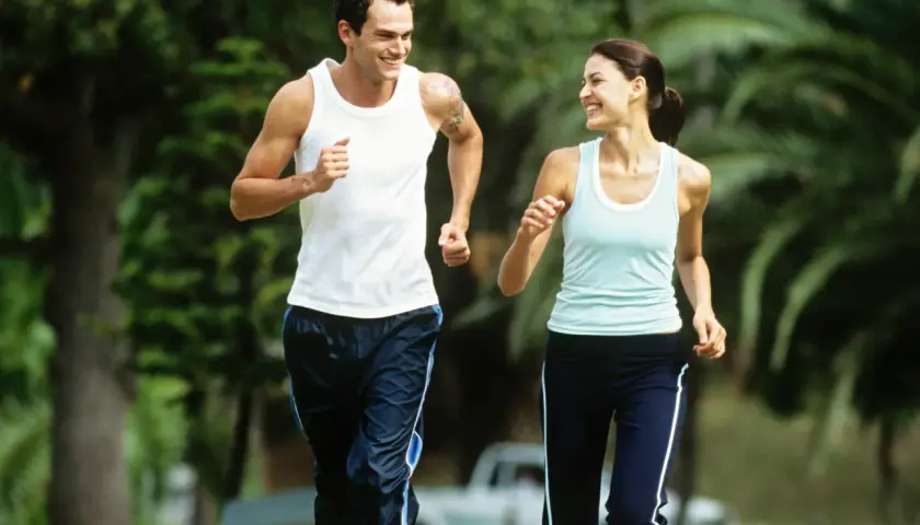 Ein Paar genießt einen Lauf im Park bei angenehmem jogging pace. Sie lachen und schauen sich an, während sie durch das Grün laufen.