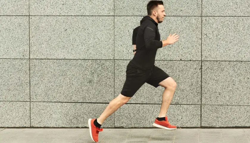 Ein Mann in Schwarz absolviert ein intensives Schwellentraining Laufen vor einer grauen Steinwand.