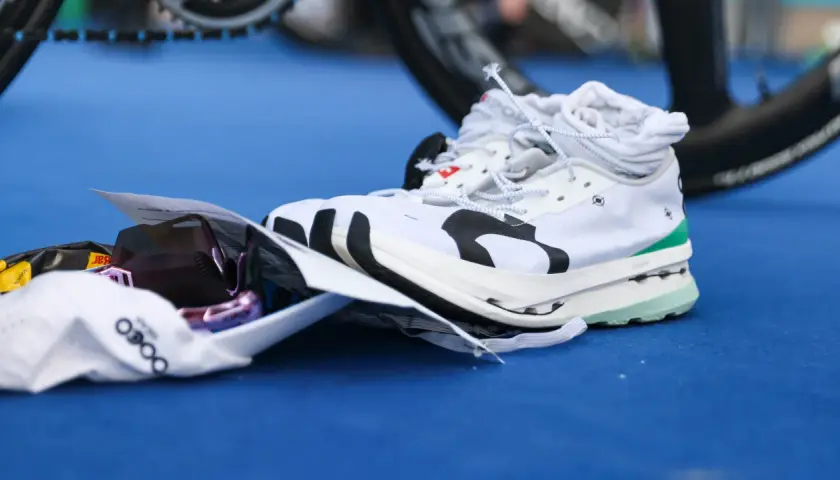 Weiße Laufschuhe mit Carbon-Sohle, bereit für den Wettkampf. Daneben liegen eine Sonnenbrille und ein Energie-Riegel.