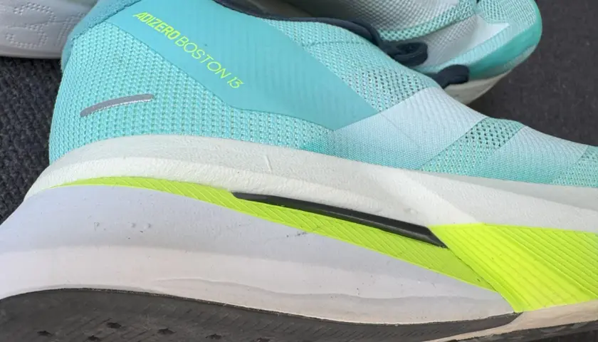Ein Laufschuh, der adidas adizero boston 13, in Türkis mit gelbem Schriftzug. Die Sohle ist weiß mit einem leuchtend grünen Akzent.