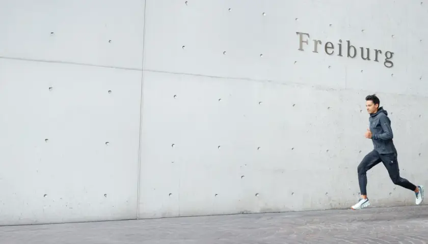 Läufer sprintet vor Betonwand mit Schriftzug "Freiburg". Bereit für den Freiburg Marathon.