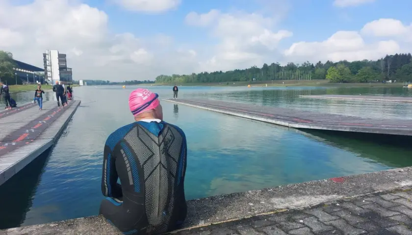 Triathlet in Neoprenanzug und Badekappe sitzt am Beckenrand und wartet auf seinen Start. Die Sonne scheint, die Bedingungen sind perfekt, um zu schwimmen.