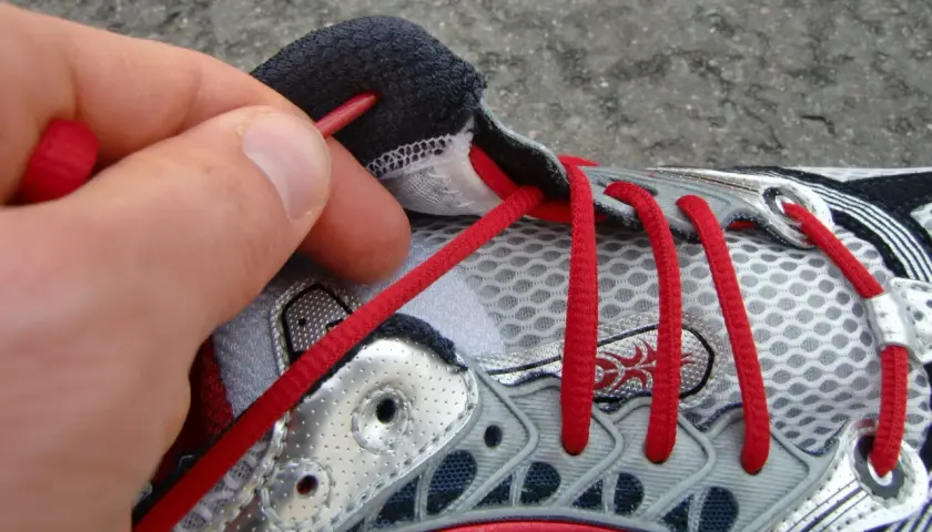 Hand zieht rote Schnürsenkel durch Ösen eines Laufschuhs. So bindet man Laufschuhe richtig für den perfekten Halt.
