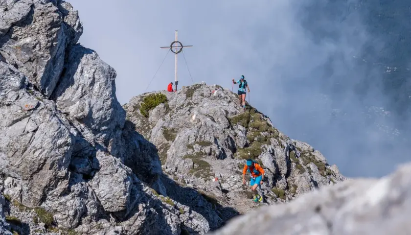 Läufer beim Tschirgant Sky Run auf felsigem Grat, Gipfelkreuz im Hintergrund.