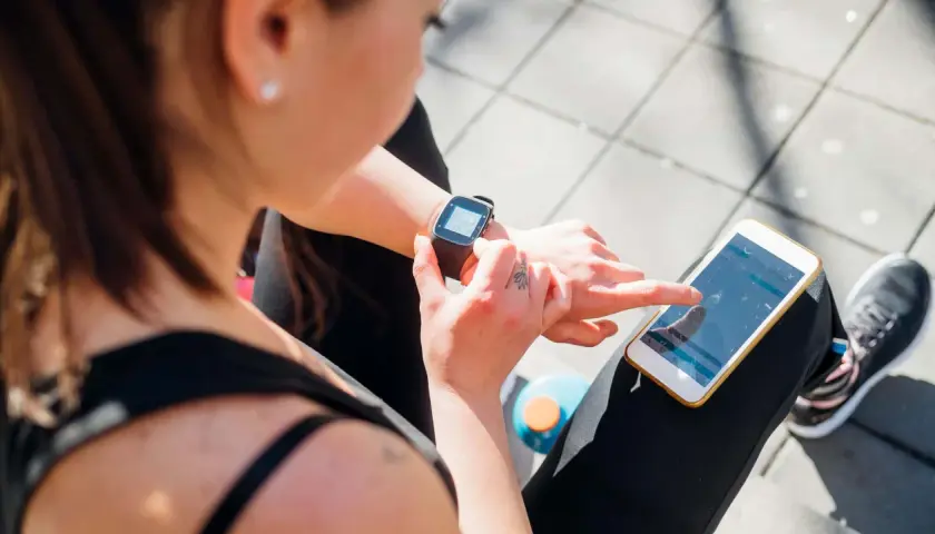 Frau prüft ihre Smartwatch und ihr Handy, um zu sehen, was ist PAI.