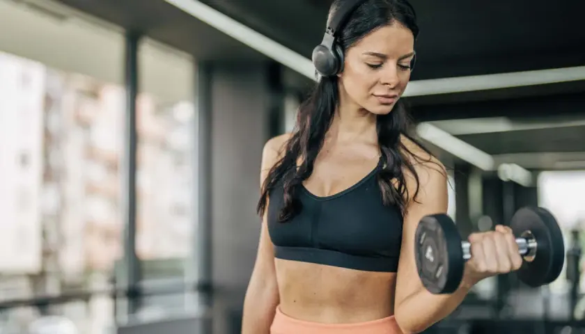Frau mit Kopfhörern hebt Hantel im Fitnessstudio. Sie fragt sich, wie oft Cardio in der Woche gut ist.