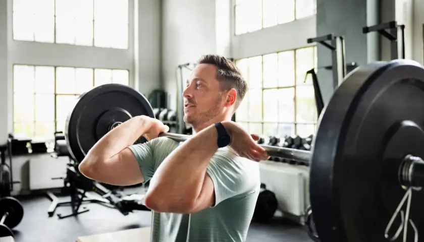 Mann hebt Langhantel im Fitnessstudio. Sein Trainingsplan 2 mal die Woche zahlt sich aus.