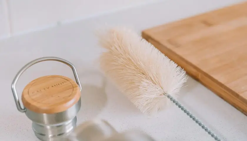 Eine Bürste liegt bereit, um die Trinkflasche zu reinigen. Daneben ein Holzbrett.