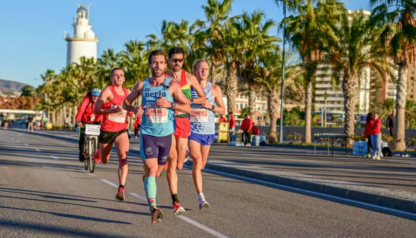 Läufer im Malaga Marathon kämpfen sich unter Palmen durch. Ein Leuchtturm im Hintergrund.