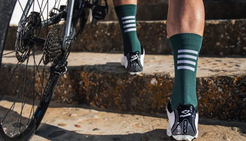 Rennradfahrer tragen lange Socken für Aerodynamik und Schutz. Hier sieht man Beine in grünen Socken mit weißen Streifen, die eine Treppe hochsteigen, neben einem Rennrad.