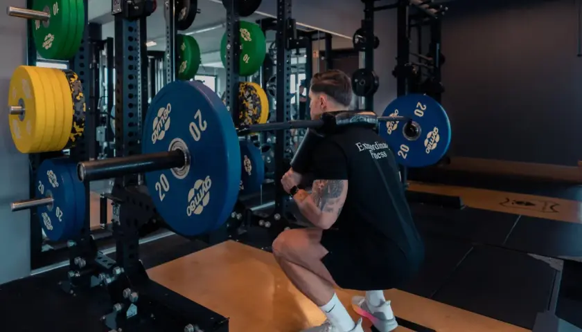 Mann macht Kniebeugen mit Langhantel. Gewichte sind gestapelt. Ein typisches Bild für ein 2er Split Push Pull Training.