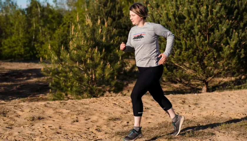 Frau beim **trail running** auf sandigem Untergrund, umgeben von Kiefern und Bäumen.