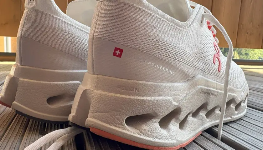Weiße Laufschuhe, On Cloudsurfer Max, mit markanter Sohle und Schweizer Kreuz-Detail.