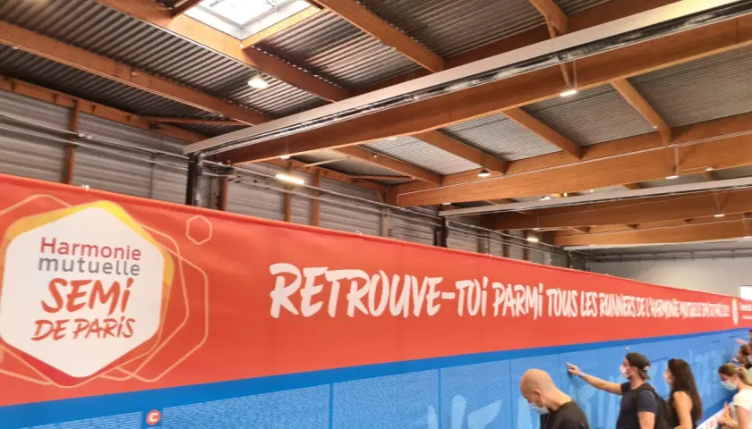 Harmonie Mutuelle SEMI DE PARIS Banner. Menschen stehen vor einer Wand mit Namen, die für den Lauf des SEMI DE PARIS werben.