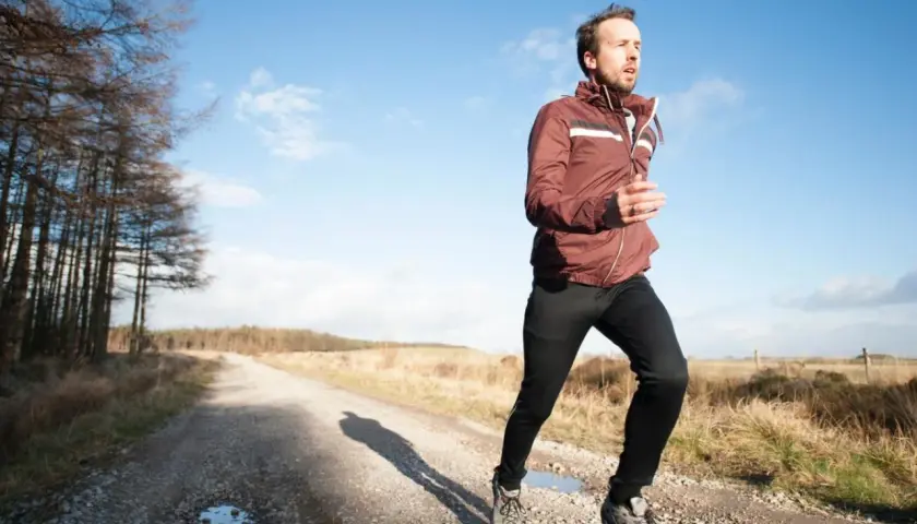 Mann joggt bei 10 Grad auf einem Feldweg. Er trägt eine leichte Jacke und lange Hose, ideal zum **was anziehen joggen 10 grad**.