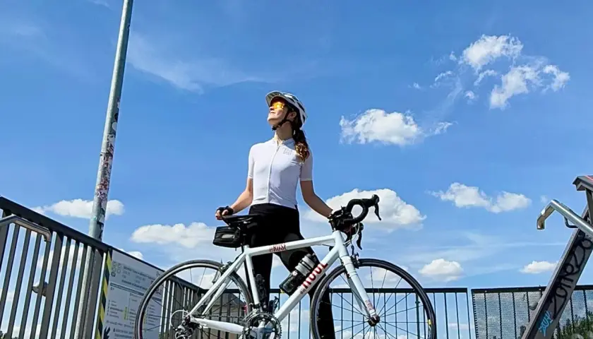 Frau mit Rennrad genießt die Sonne nach einem intensiven Intervalltraining Fahrrad. Blauer Himmel mit Wolken.