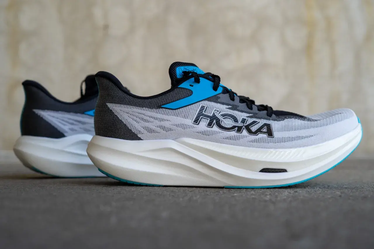 Zwei Hoka Rocket X3 Laufschuhe in Grau mit blauen Akzenten und weißer Sohle stehen nebeneinander.