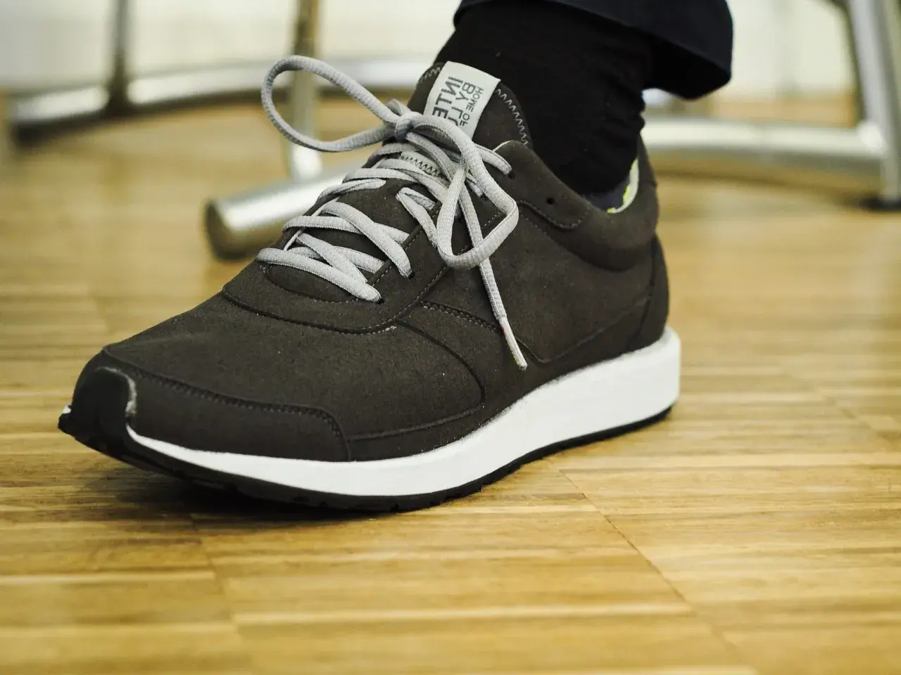 Dunkelgrauer Sneaker mit weißen Schnürsenkeln auf Holzfußboden. Gute Lunge Schuhe Erfahrungen für den Alltag.