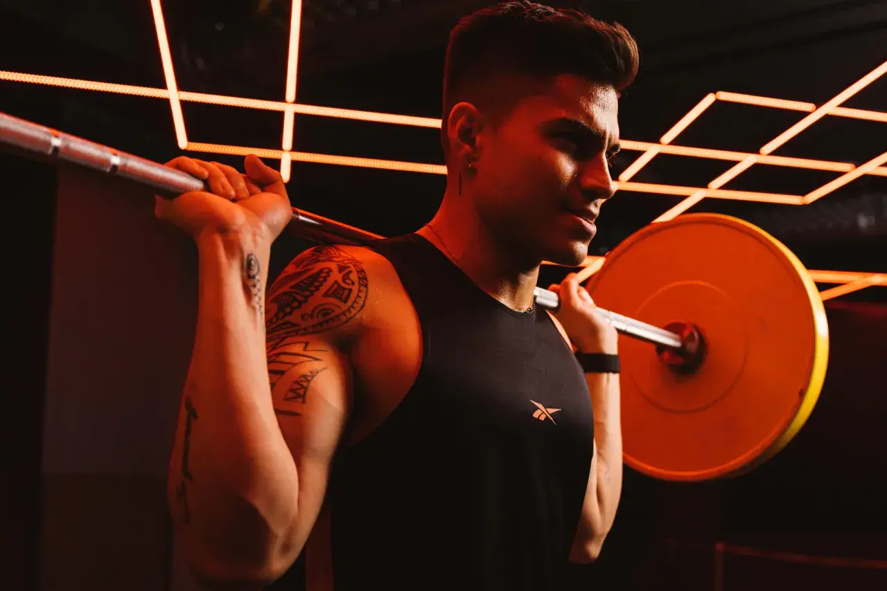 Ein Mann mit Tattoos und einem schwarzen Tanktop hebt eine Hantel. Er schwitzt und konzentriert sich auf sein Dropsatz Training.