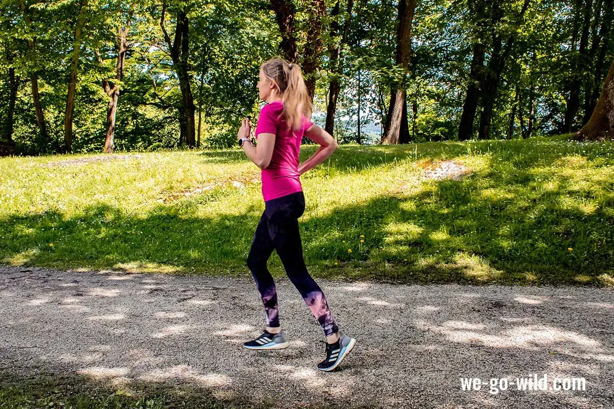 Frau läuft im Wald, um sich aufzulaufen. Sonnenschein und grüne Bäume schaffen eine idyllische Kulisse für ihr Training.