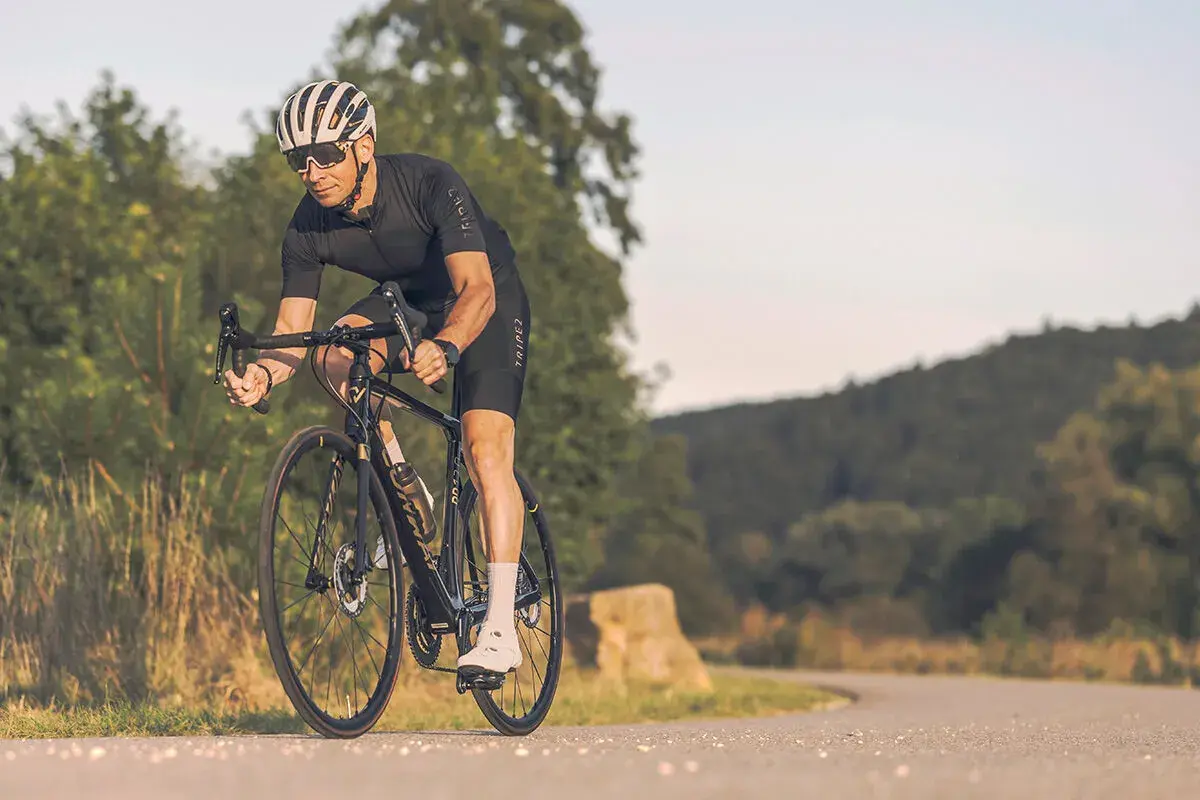 Mann auf Rennrad mit Helm und Brille fährt auf asphaltierter Straße durch hügelige Landschaft. Tolle Rennrad Tipps für deine nächste Tour!