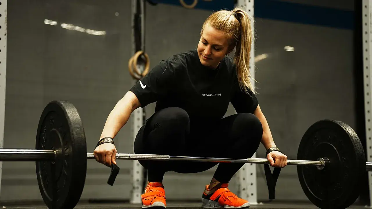 Eine Frau im Fitnessstudio bereitet sich auf das Gewichtheben vor. Eine Woche Trainingspause kann sinnvoll sein, um sich zu erholen.