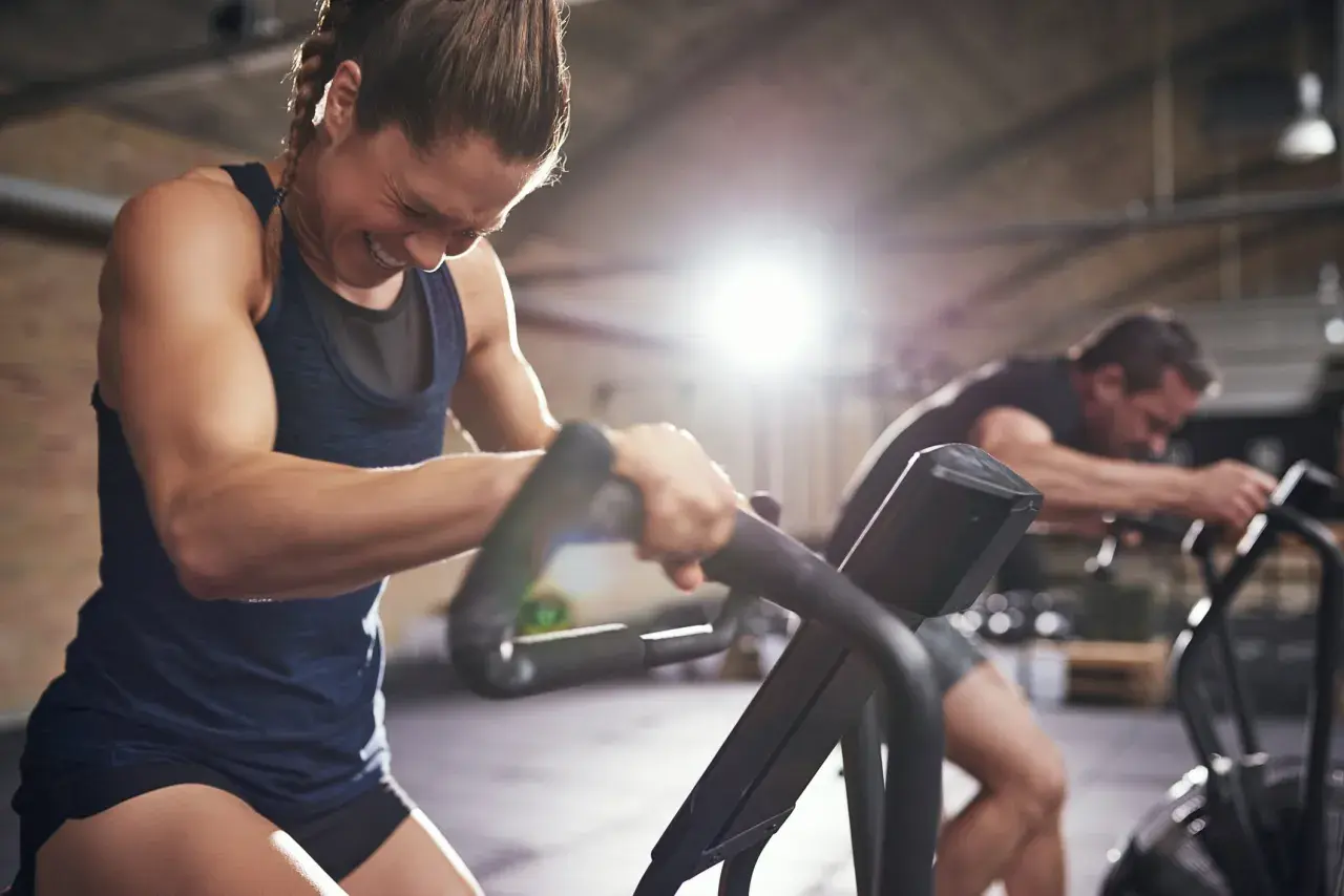 Frau kämpft auf einem Trainingsgerät, während ein Mann im Hintergrund trainiert. Selbst an trainingsfreien Tagen ist Disziplin gefragt.