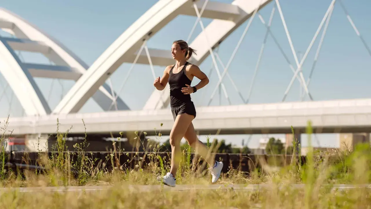 Frau joggt unter einer modernen Brücke. Sie fragt sich, wie oft joggen in der Woche gesund ist.
