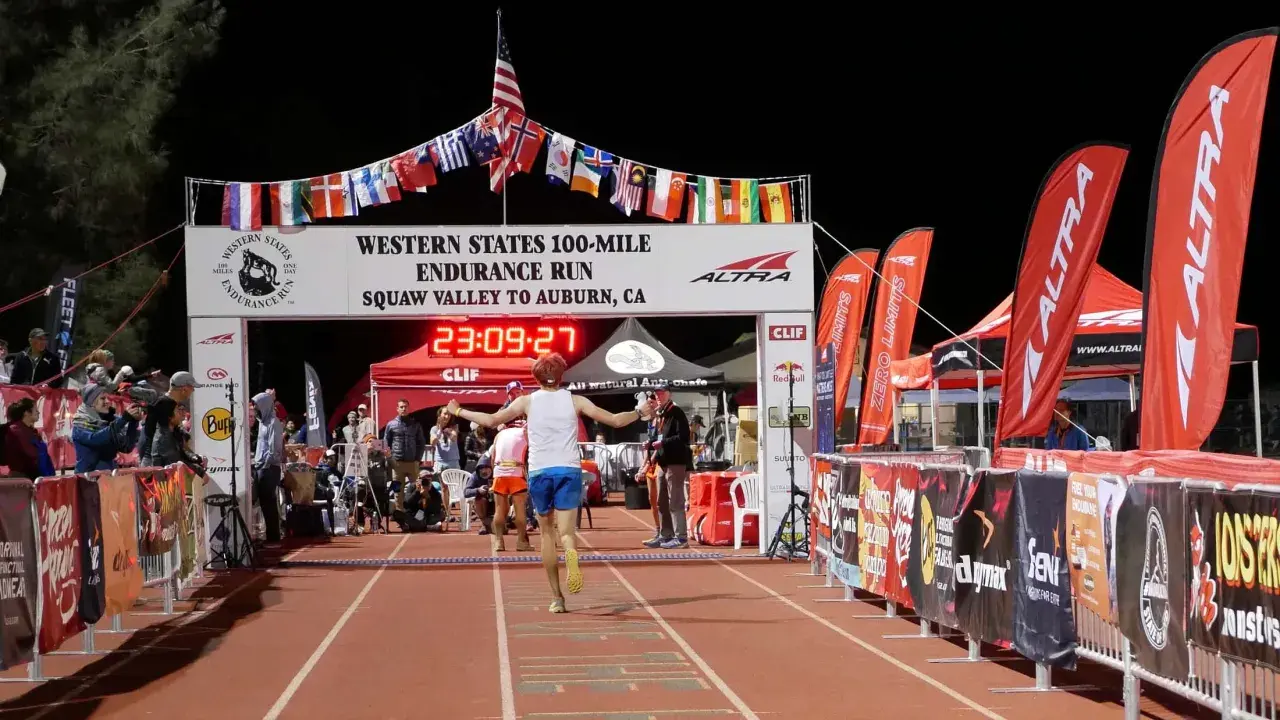 Läufer erreicht das Ziel beim Western States 100-Mile Endurance Run. Die Ziellinie ist mit Flaggen geschmückt, die an einen Ultramarathon in Deutschland erinnern.