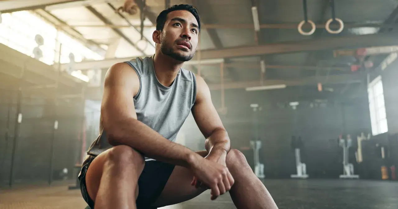 Mann im Fitnessstudio, nachdenklich nach dem Krafttraining. Er fragt sich, ob Cortison eine Rolle spielen könnte.