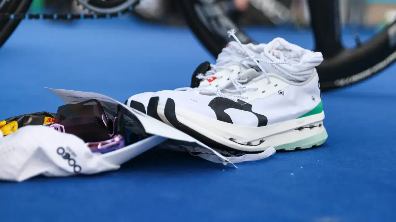 Weiße Laufschuhe mit Carbon-Sohle, bereit für den Wettkampf. Daneben liegen eine Sonnenbrille und ein Energie-Riegel.