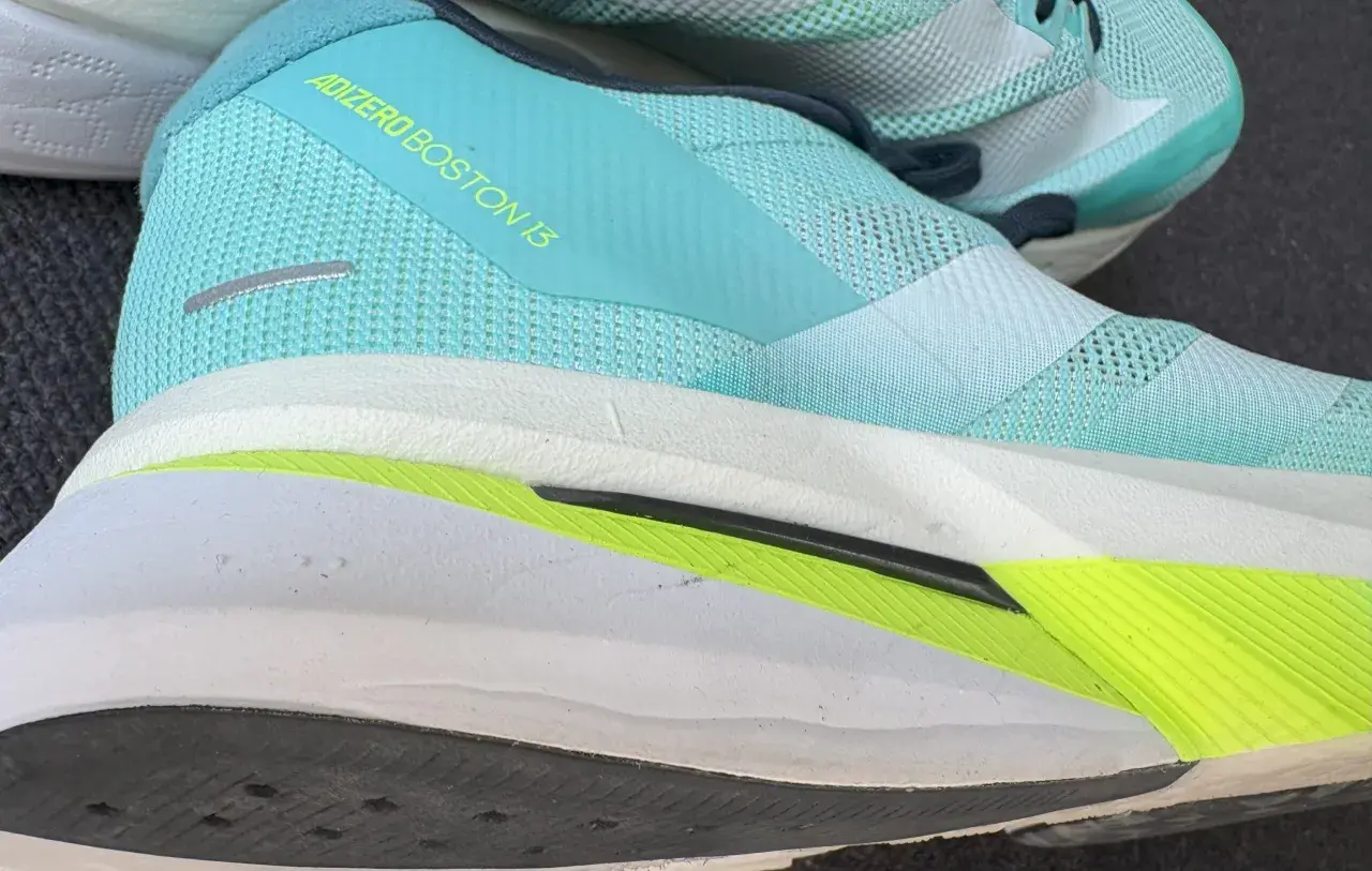 Ein Laufschuh, der adidas adizero boston 13, in Türkis mit gelbem Schriftzug. Die Sohle ist weiß mit einem leuchtend grünen Akzent.