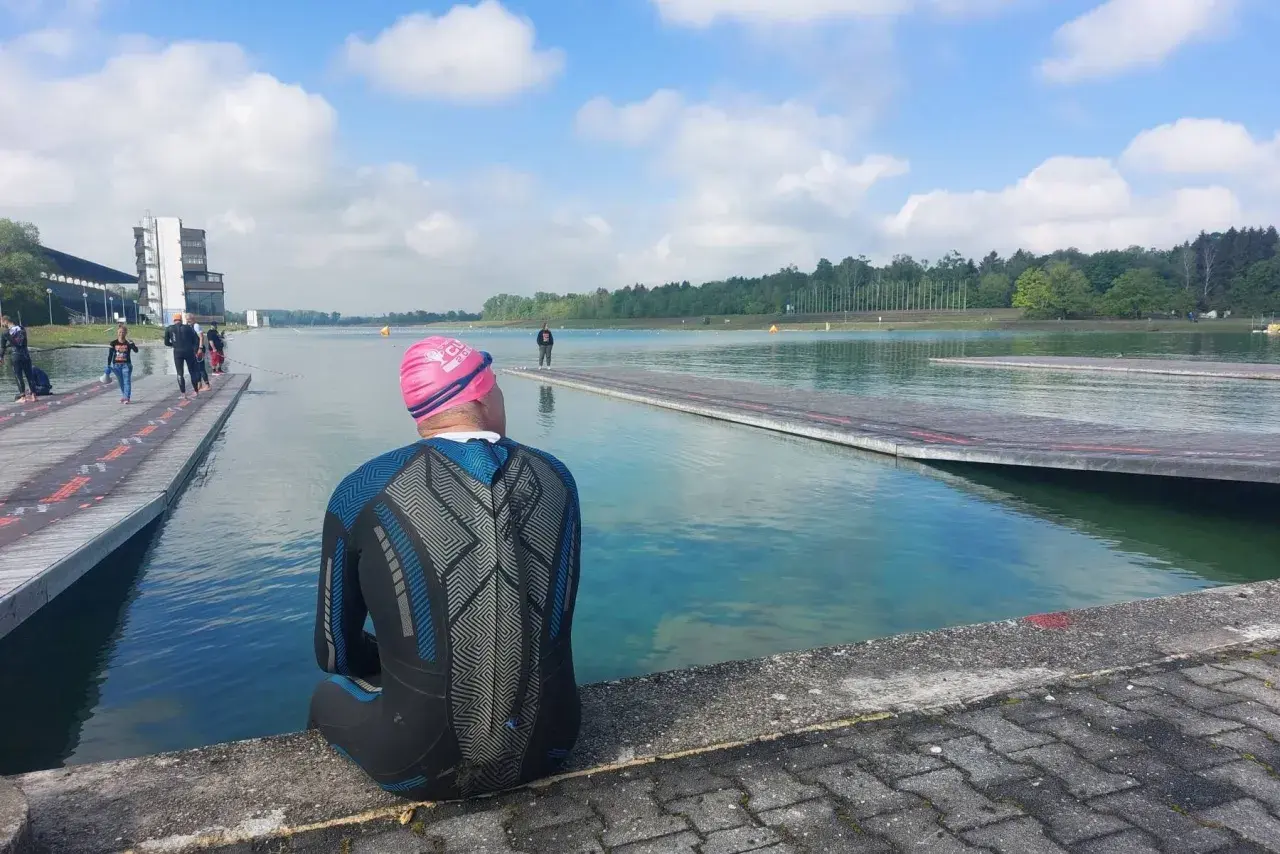 Triathlet in Neoprenanzug und Badekappe sitzt am Beckenrand und wartet auf seinen Start. Die Sonne scheint, die Bedingungen sind perfekt, um zu schwimmen.