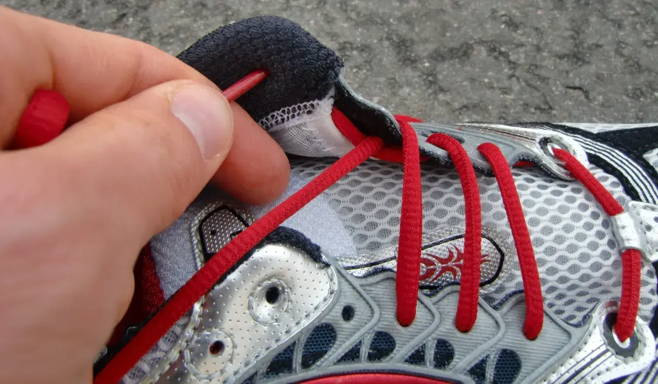 Hand zieht rote Schnürsenkel durch Ösen eines Laufschuhs. So bindet man Laufschuhe richtig für den perfekten Halt.