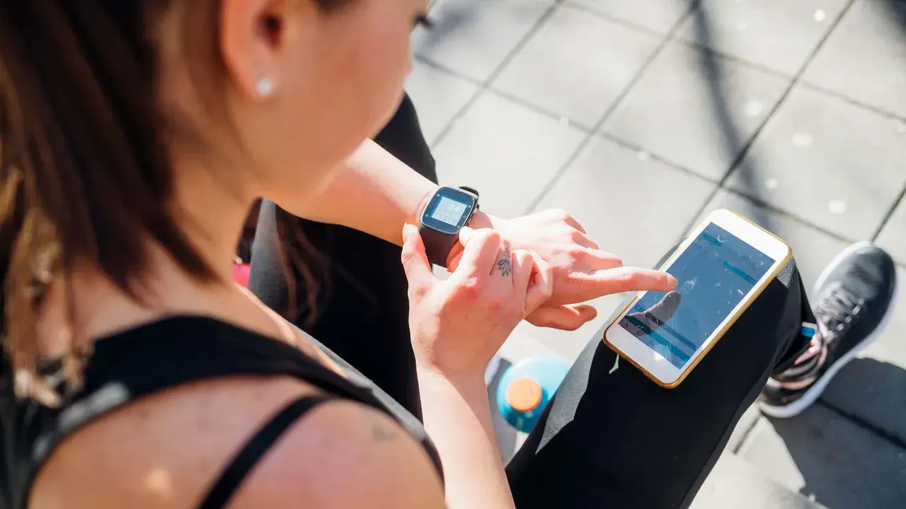Frau prüft ihre Smartwatch und ihr Handy, um zu sehen, was ist PAI.