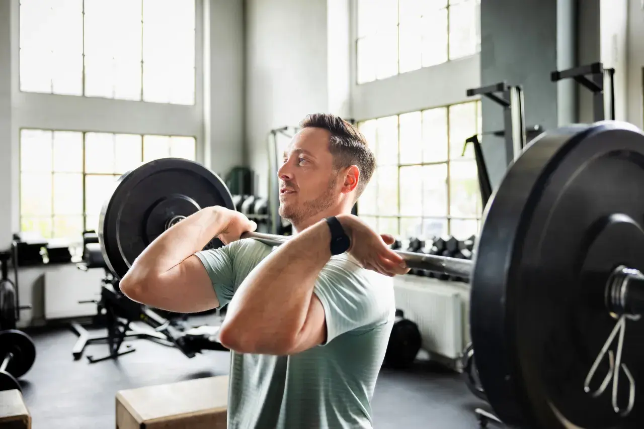 Mann hebt Langhantel im Fitnessstudio. Sein Trainingsplan 2 mal die Woche zahlt sich aus.