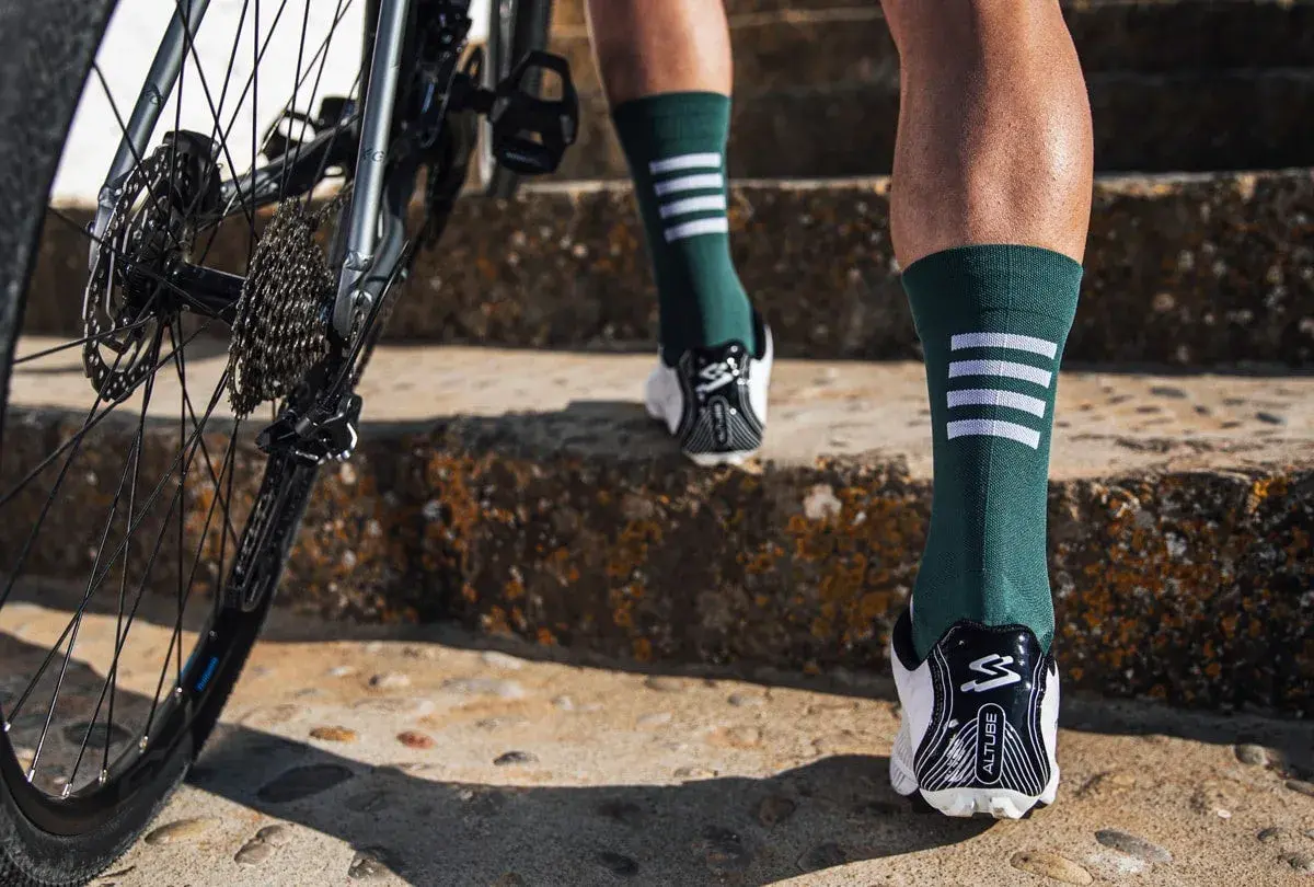 Rennradfahrer tragen lange Socken für Aerodynamik und Schutz. Hier sieht man Beine in grünen Socken mit weißen Streifen, die eine Treppe hochsteigen, neben einem Rennrad.