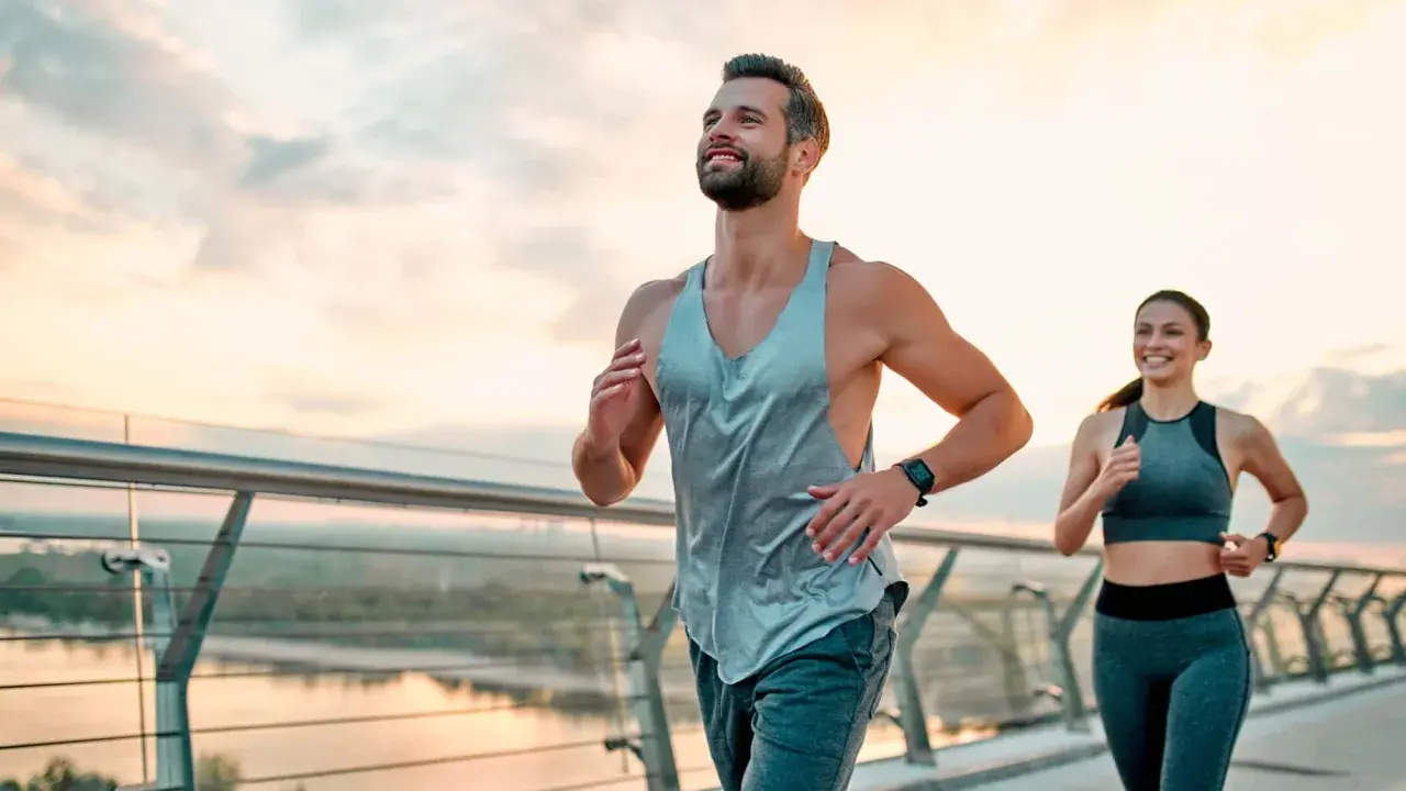 Ein Paar joggt auf einer Brücke bei Sonnenaufgang. Sie folgen einem ausgewogenen joggen und krafttraining wochenplan für ihre Fitness.